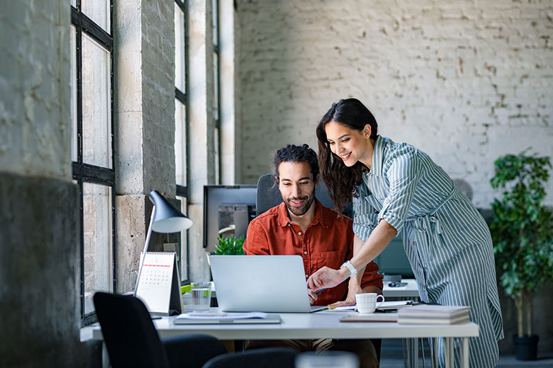 Two co-workers huddle over a laptop in the office