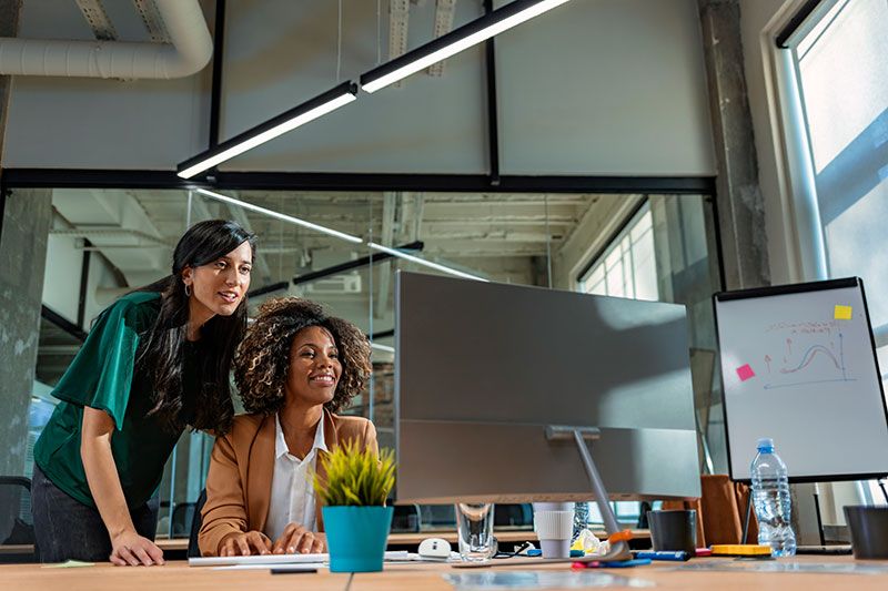 Two co-workers in a modern office look at a large computer monitor