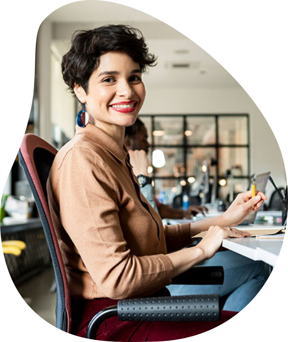 A professional woman smiles and sits at a desk in a modern office